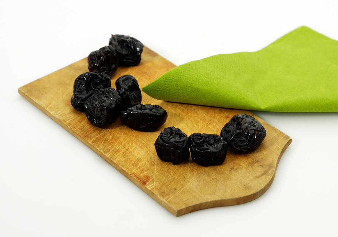 Dry plums on wooden platter with green cloth on white background