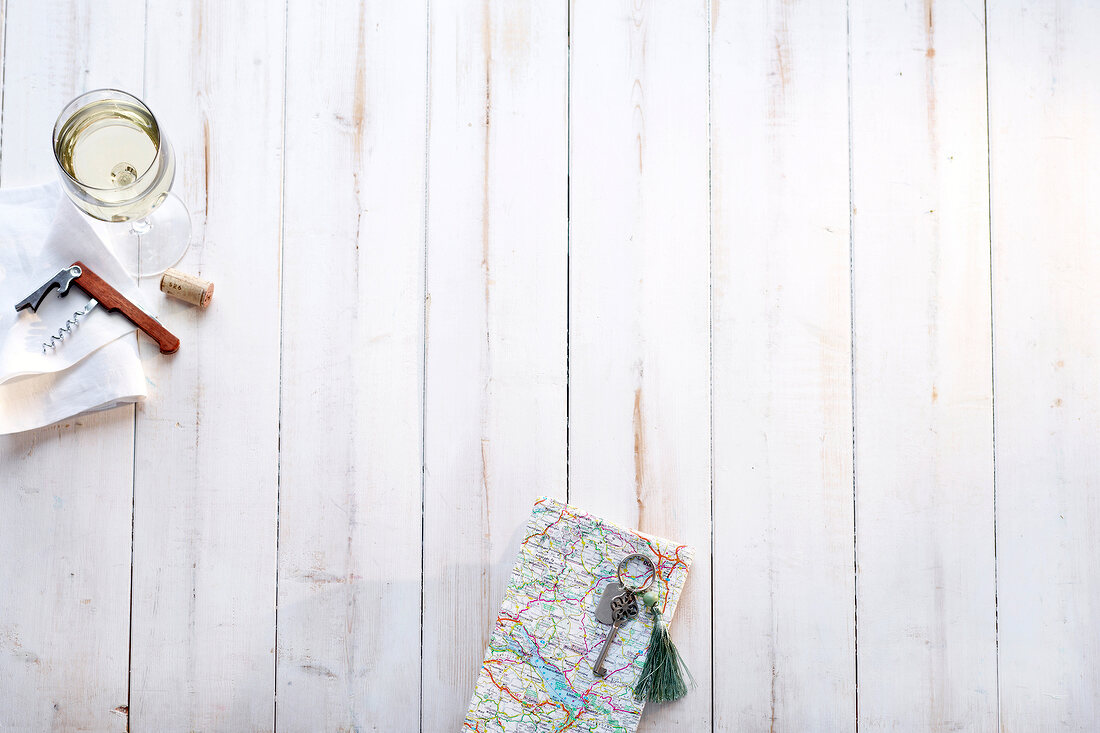 Road map, key, wine glass and bottle opener on wooden background