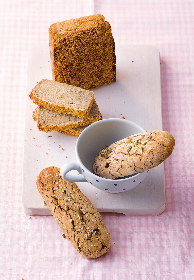 Gluten free quinoa bread and pumpkin seed bun in cup and on chopping board