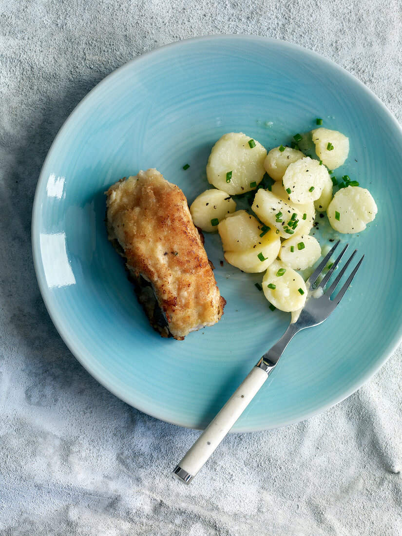 Close-up of baked fish fillet with potato salad on plate