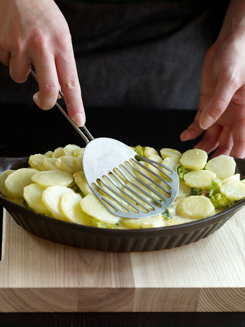 Close-up of hand smashing potatoes and broccoli with spatula, step 3