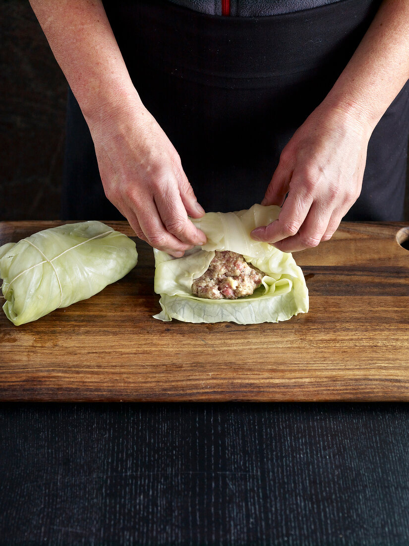 Close-up of hand rolling stuffed cabbage on wooden board, step 2