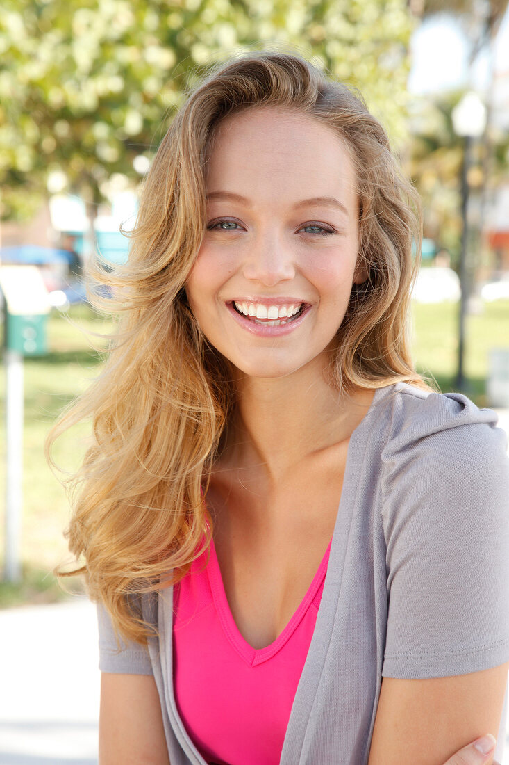 Portrait of beautiful blonde woman wearing pink and gray top, smiling