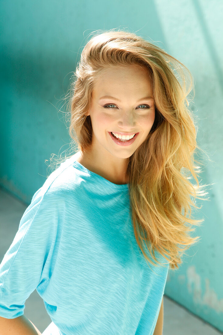 Portrait of beautiful blonde woman wearing turquoise top, smiling