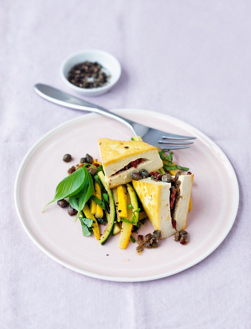Tofu filled with capers on bed of green and yellow courgettes strips