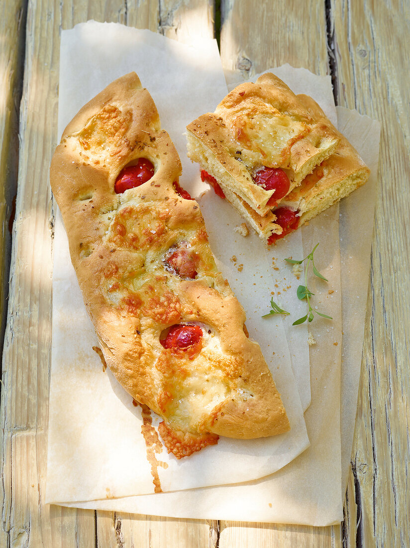 Loaf and pieces of focaccia with potatoes, tomatoes and oregano