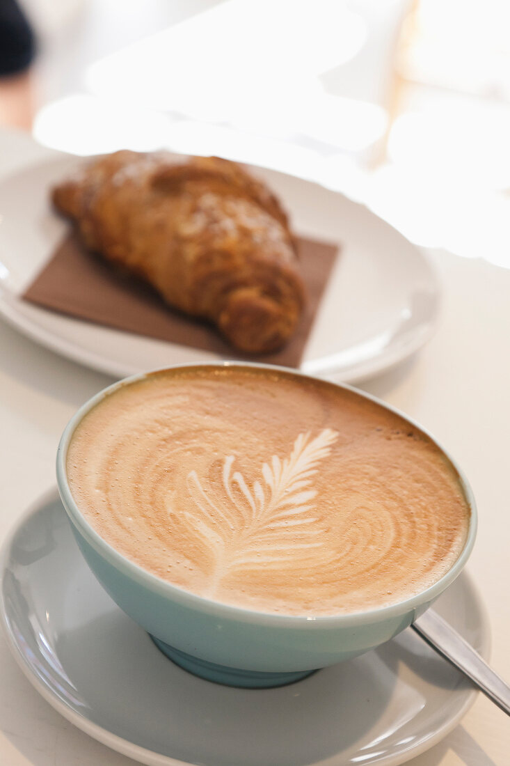 Close-up of cup of coffee with croissant on plate