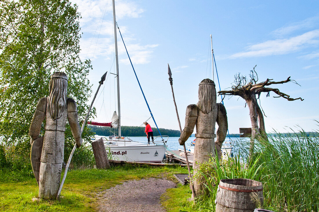 Two wooden sculptures in front of lake in Galindia Mazurski Eden, Warmia Masuria, Poland