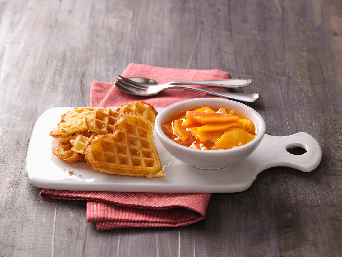 Heart shaped waffles with bowl of mango and papaya compote on tray