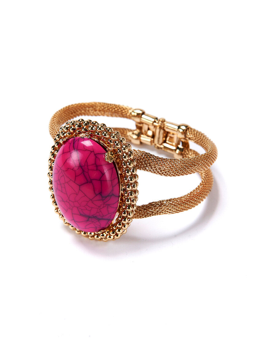 Close-up of golden bangle with pink gemstone on white background