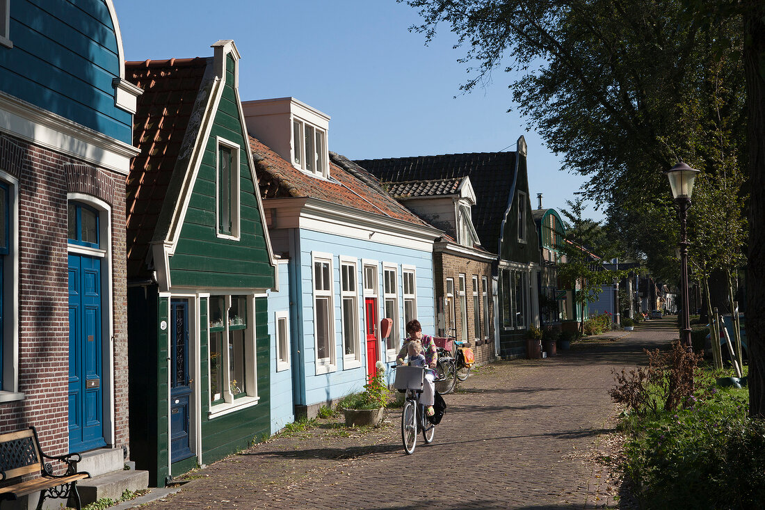 Woman cycling on road beside old captain's houses in Buiksloterdijk, Noord, Amsterdam