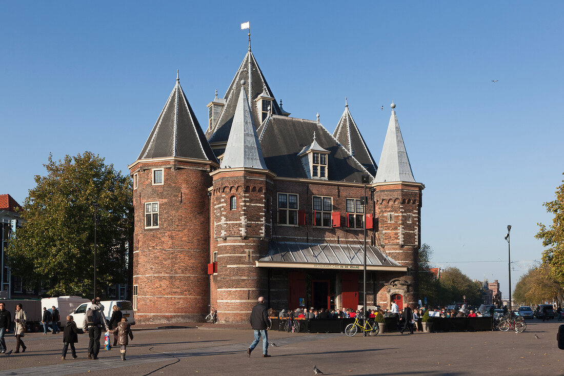 Tourists standing and cycling outside Waag monument in Nieuwmarkt, Amsterdam, Netherlands