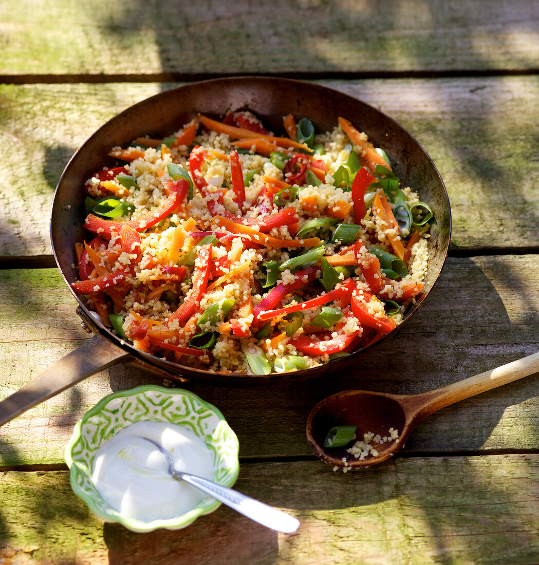 Couscous in frying pan with yogurt dip in bowl