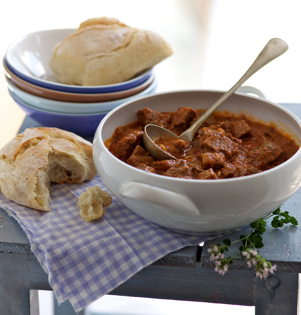 Beef stew in pot with crusty rolls on table