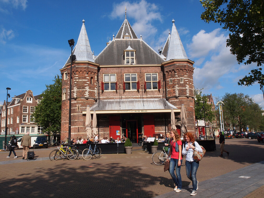 Tourists standing and cycling outside Waag monument in Nieuwmarkt, Amsterdam, Netherlands