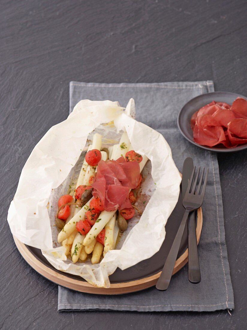 White asparagus with cherry tomatoes, capers and bresaola on parchment paper