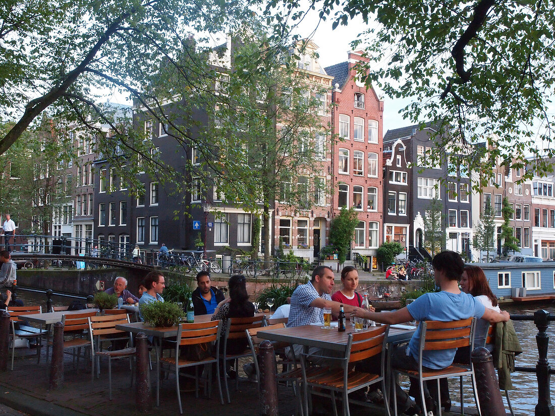 People at cafe on pavement with canal houses in background, Amsterdam, Netherlands