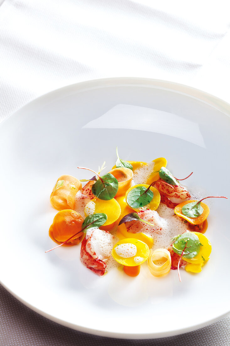 Lobster with carrots, lime, young herbs and spice foam on plate