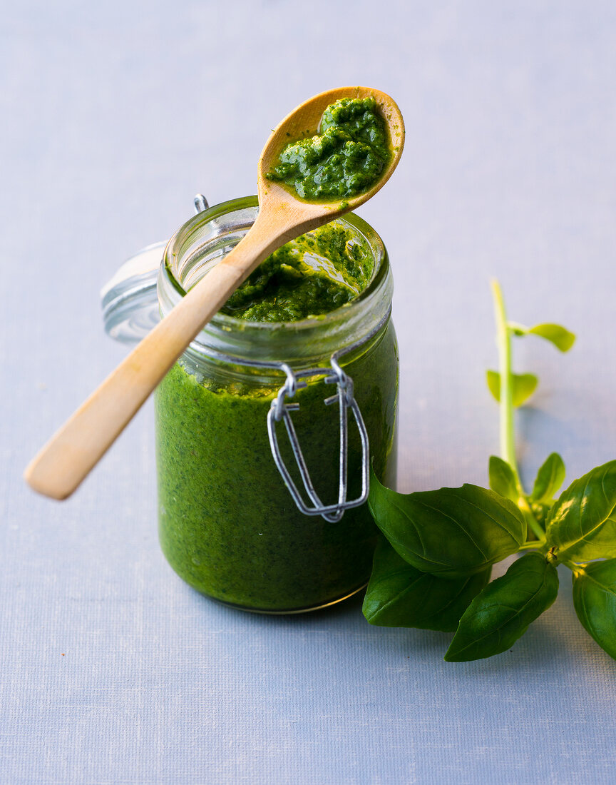 Glass jar of basil pesto with wooden spoon on top