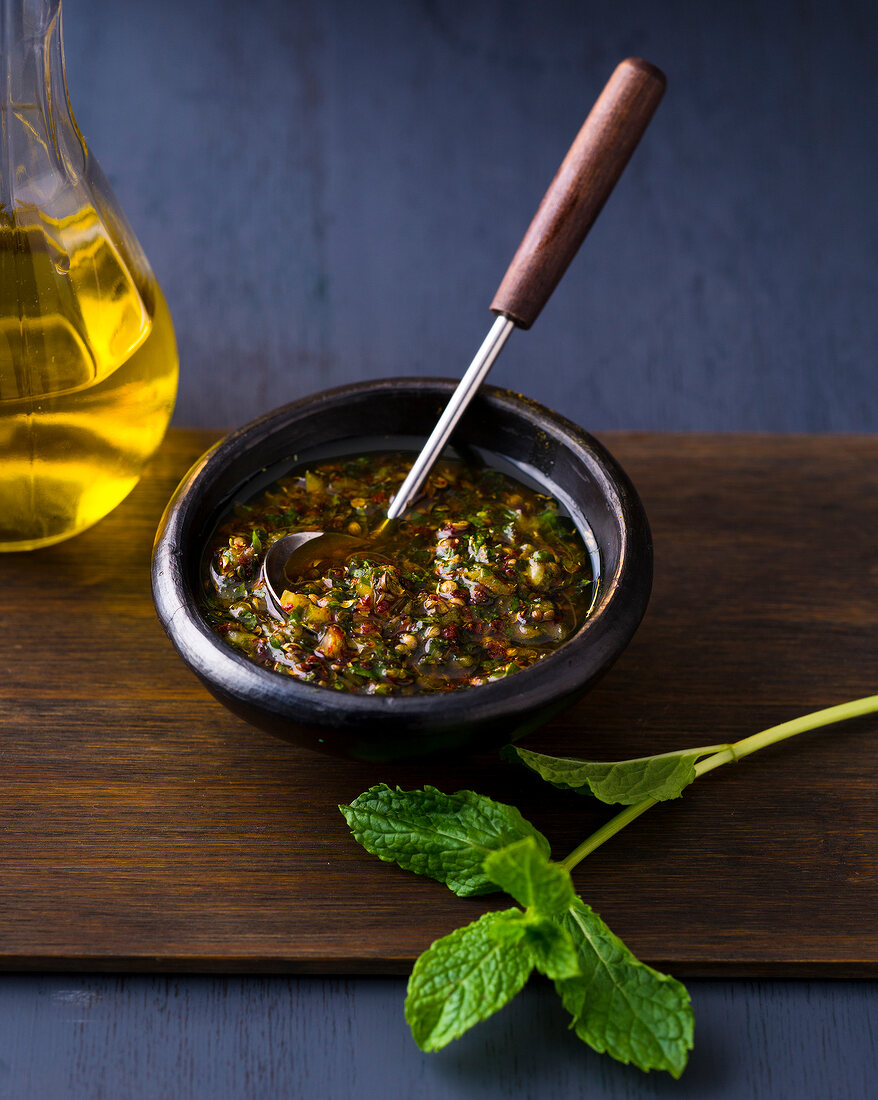 Bowl of mint chermoula with spoon on wooden board