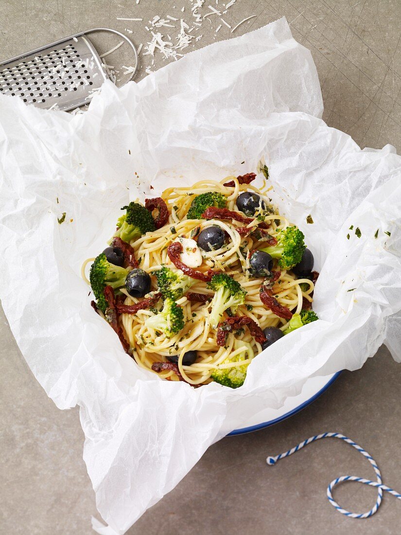 A spaghetti nest in parchment paper with olives, broccoli and dried tomatoes