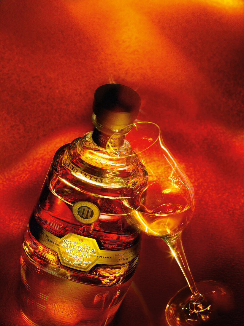 Tequila bottle and glass on red background