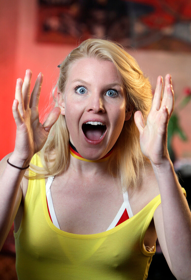 Portrait of ecstatic blonde woman wearing yellow tank top gesturing, screaming