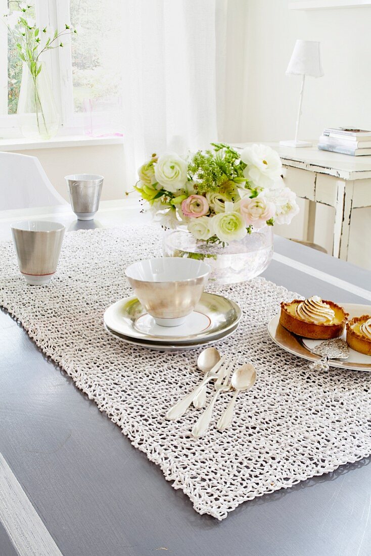 A table laid for coffee with a net-like table runner and bunch of flowers