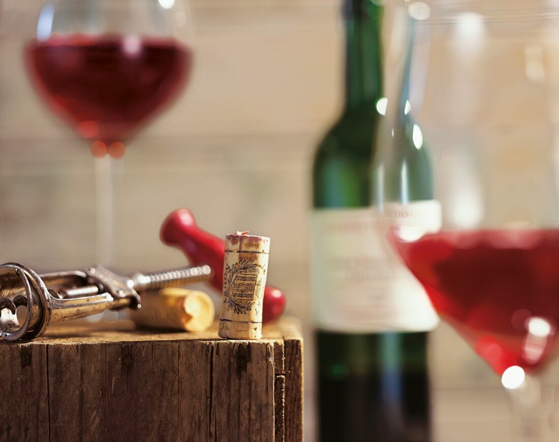A corkscrew, corks, a bottle of wine and glasses of red wine