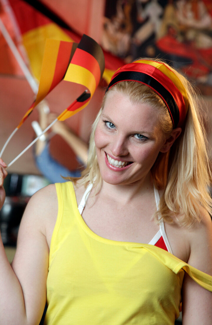 Happy blonde woman wearing yellow tank top holding German flags, laughing
