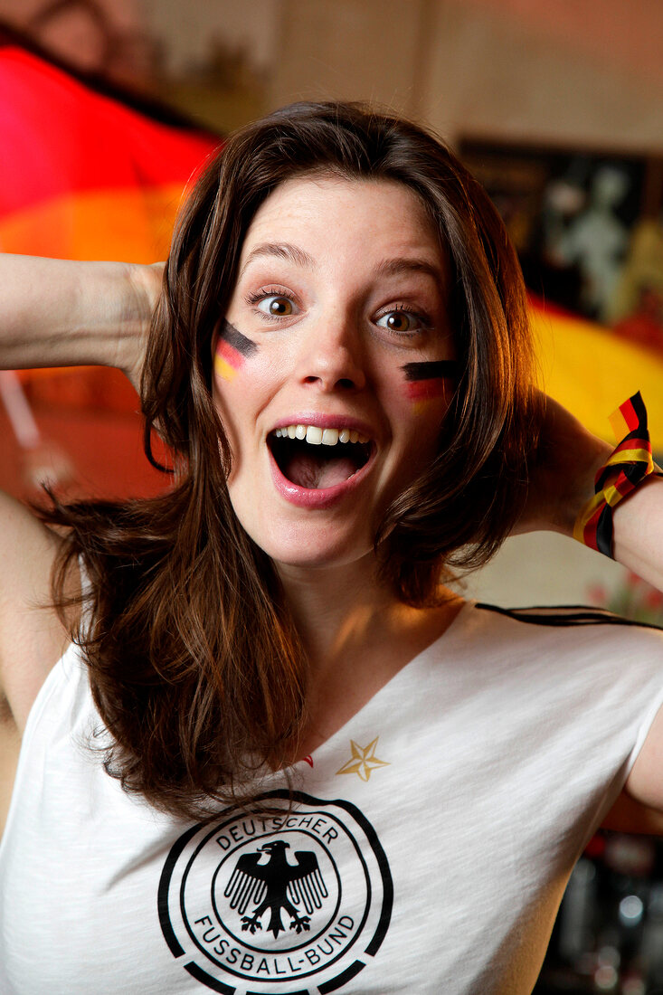 Excited brunette woman wearing white German jersey and flag painted on cheek, laughing