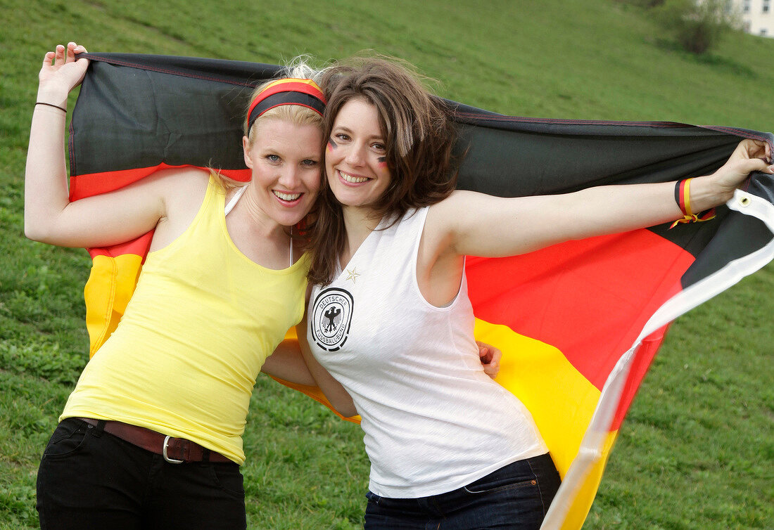 Portrait of two beautiful women holding German flag and smiling