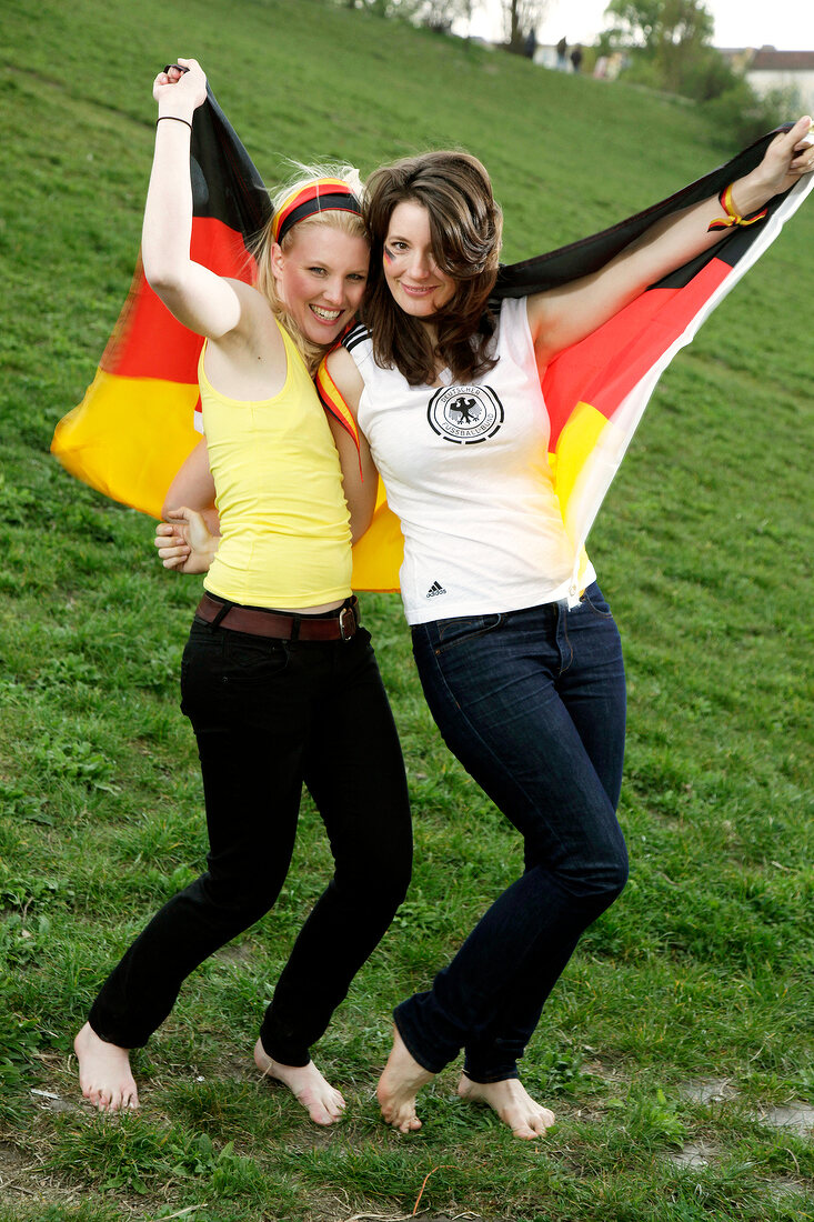 Portrait of two beautiful woman holding Germany flag behind them