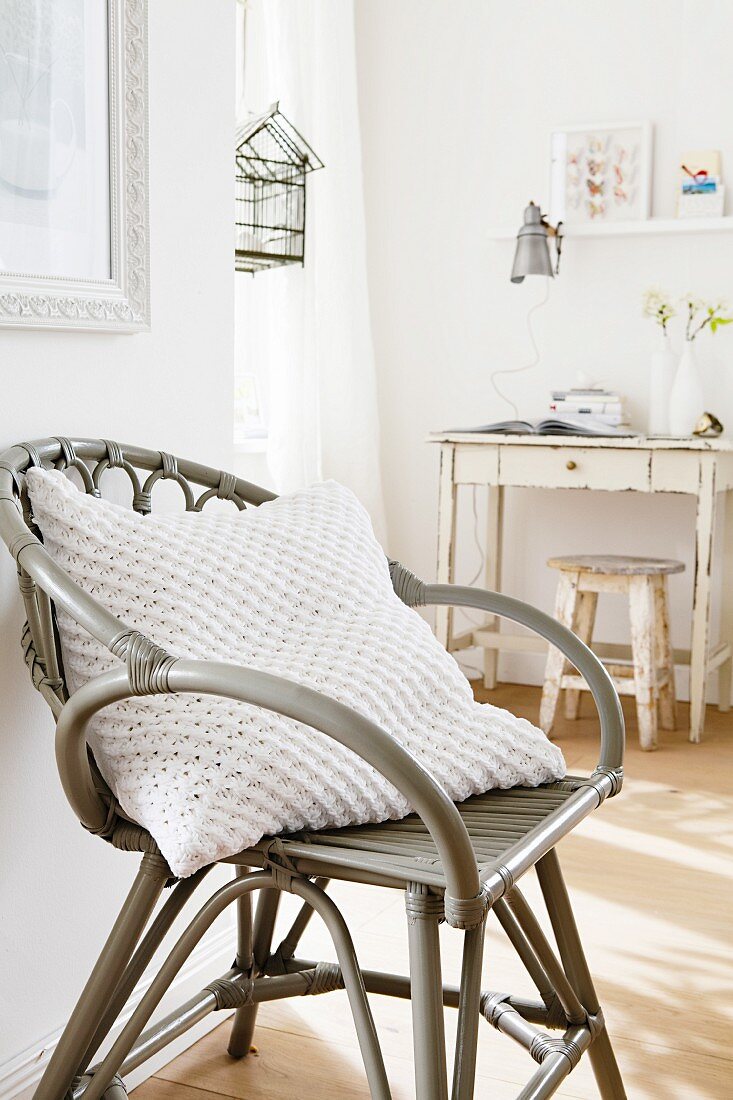 A cushion with a white knitted cover on a wicker chair
