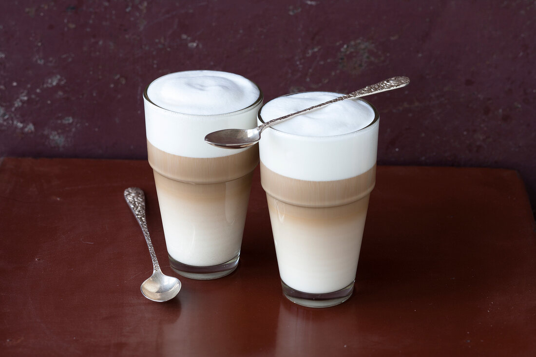 Glasses of latte macchiato with spoons on brown background