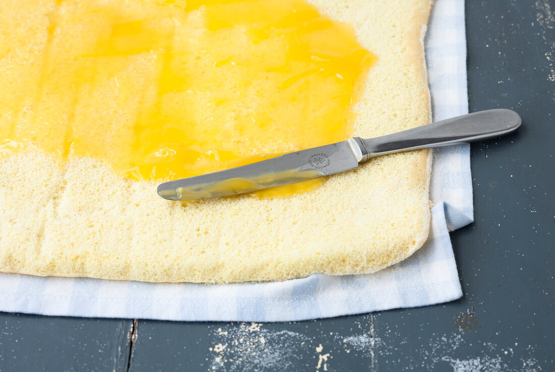 Lemon curd being spread on sponge base for preparation of cheese cake, step 3