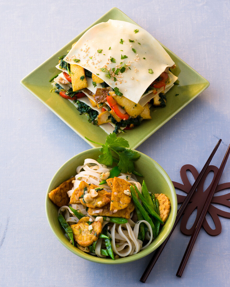 Rice noodles with tempeh in bowl and Asia lasagne on plate