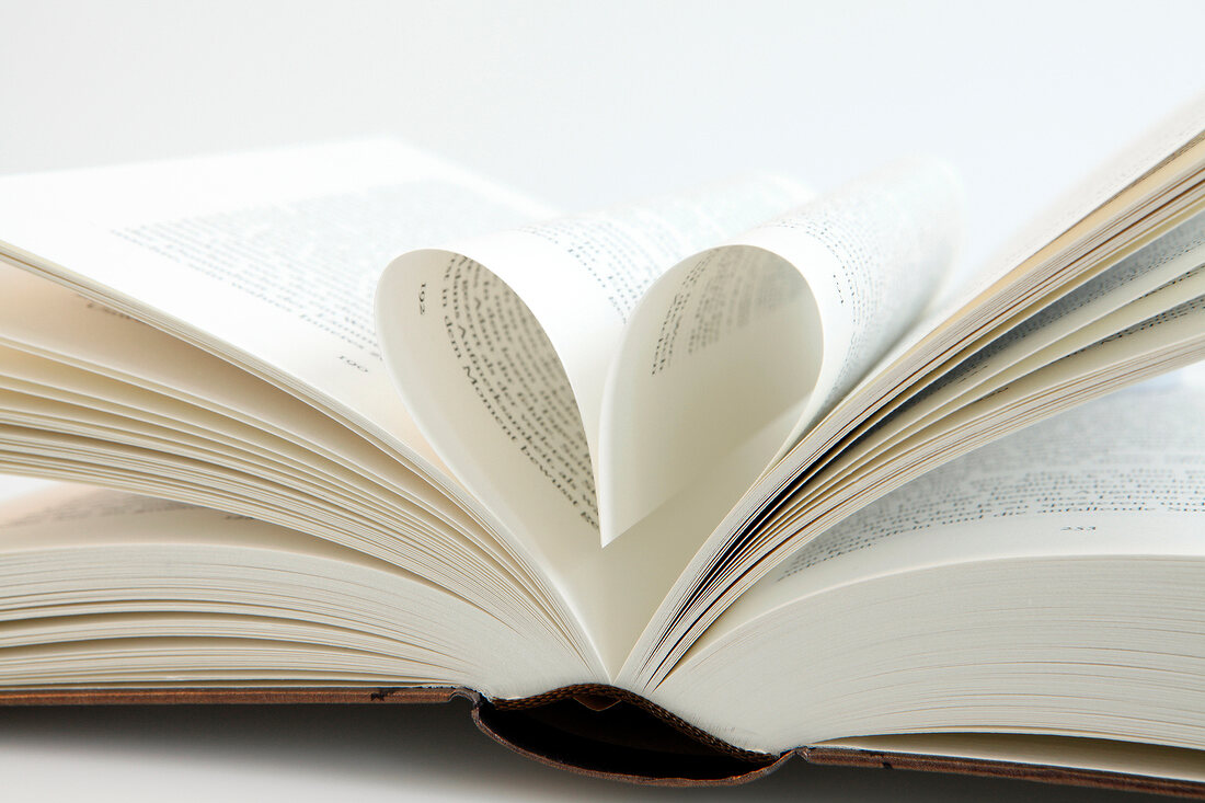 Close-up of open book with pages folded in heart shape on white background