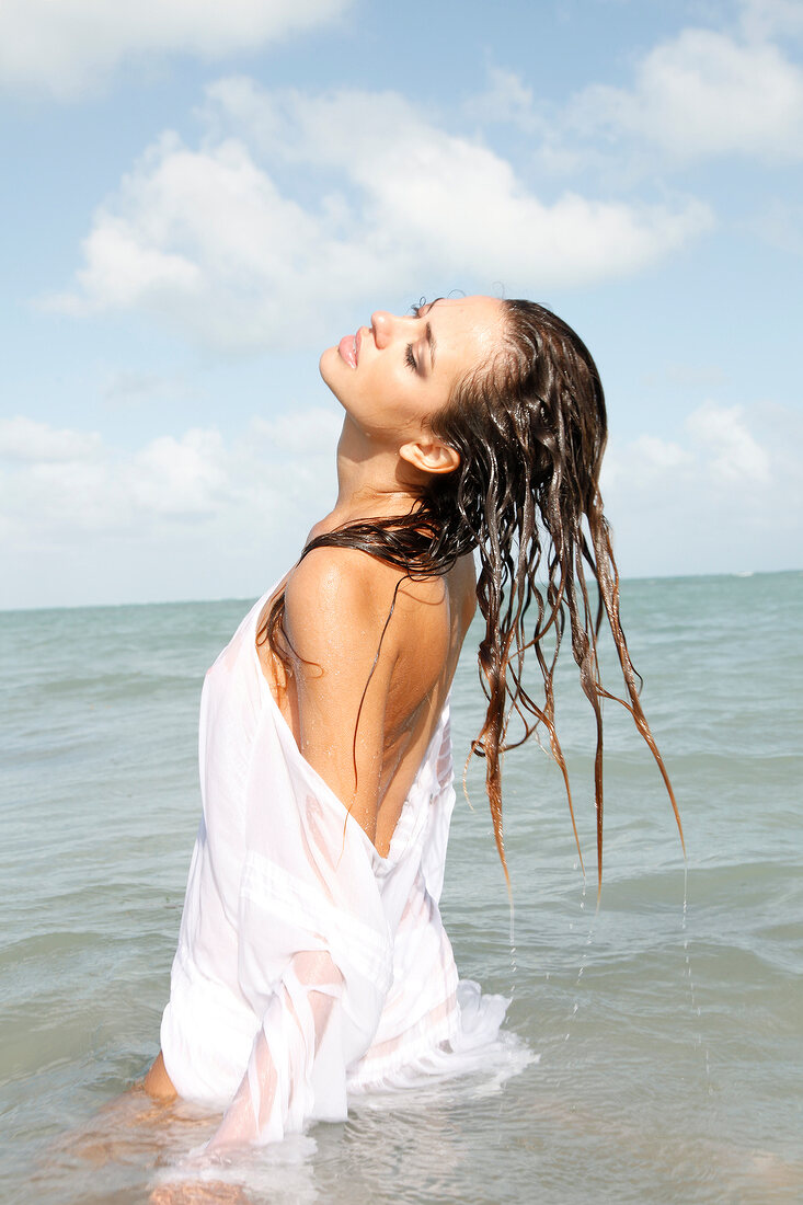 Frau mit langen braunen Haaren in weißem Hemd im Meer