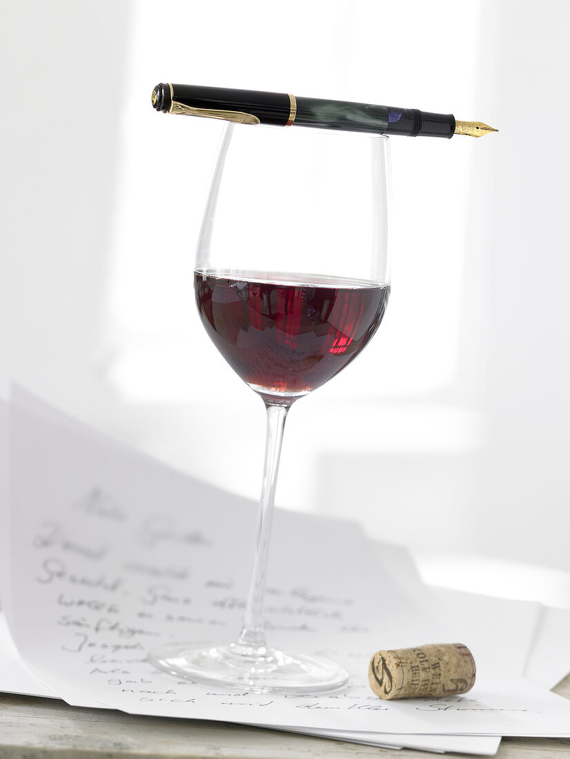 Glass of red wine with pen, letter and cork