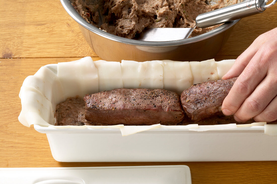 Venison fillets being placed on stuffing and bacon slices in baking dish, step 2