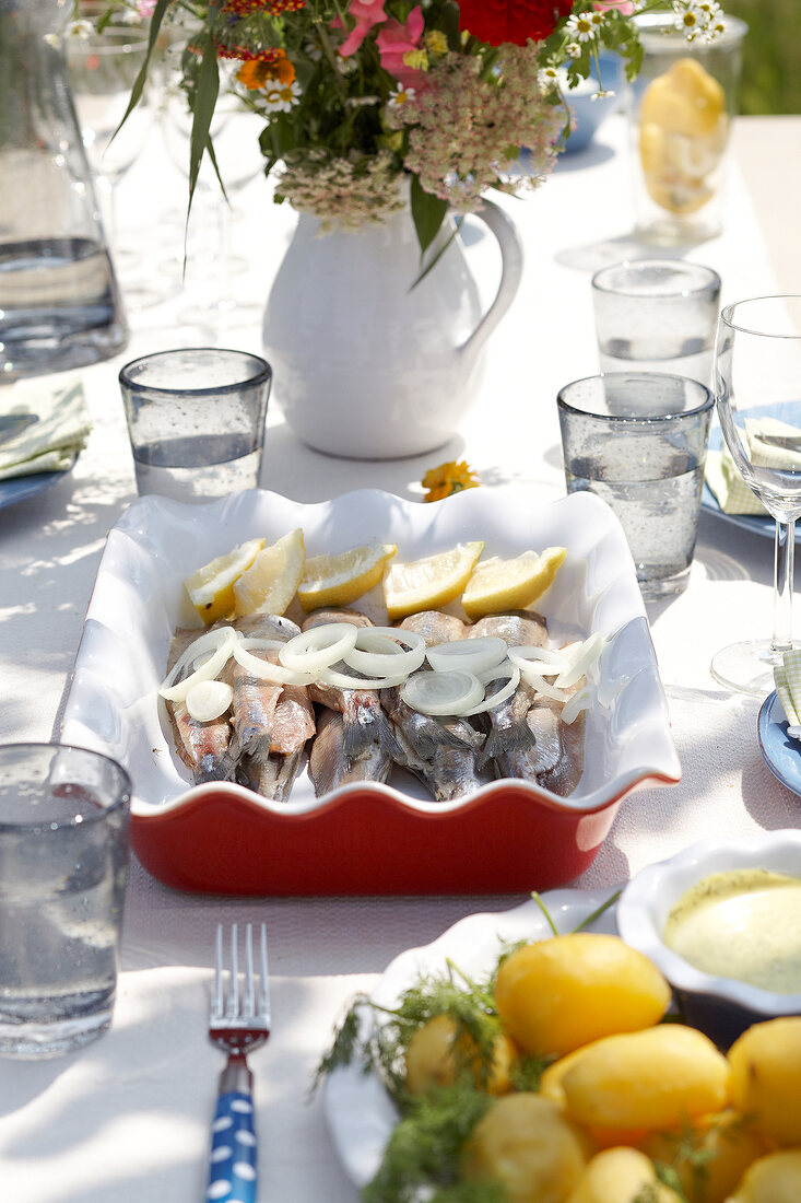 Herring on serving tray with glasses and flower vase on table