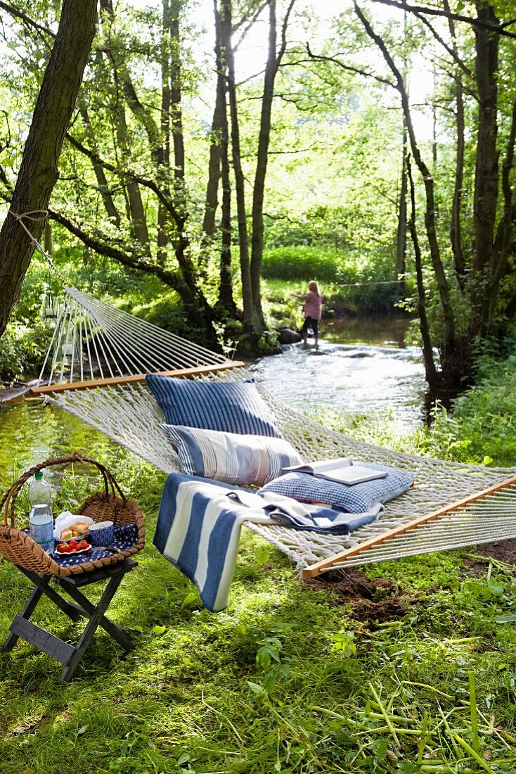 Cushions in a hammock and a picnic basket on a stool in a forest