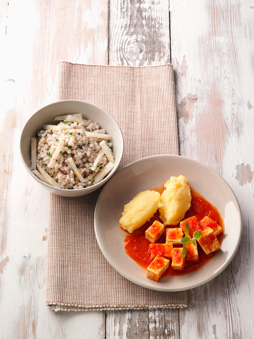 Plate of Jerusalem artichokes with goulash and bowl of soy meat and Pearl barley on table