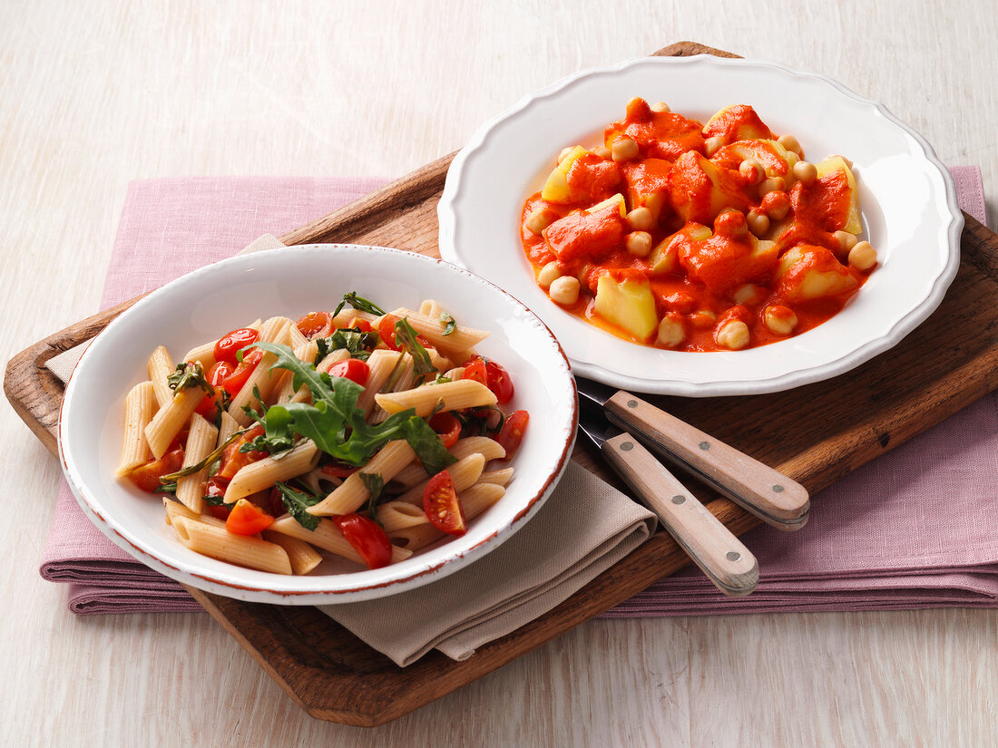 Close-up of pasta with cherry tomatoes and potato goulash in dishes on serving tray