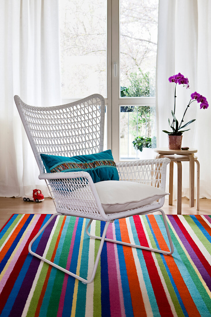 White wicker chair with cushion on colourful striped carpet