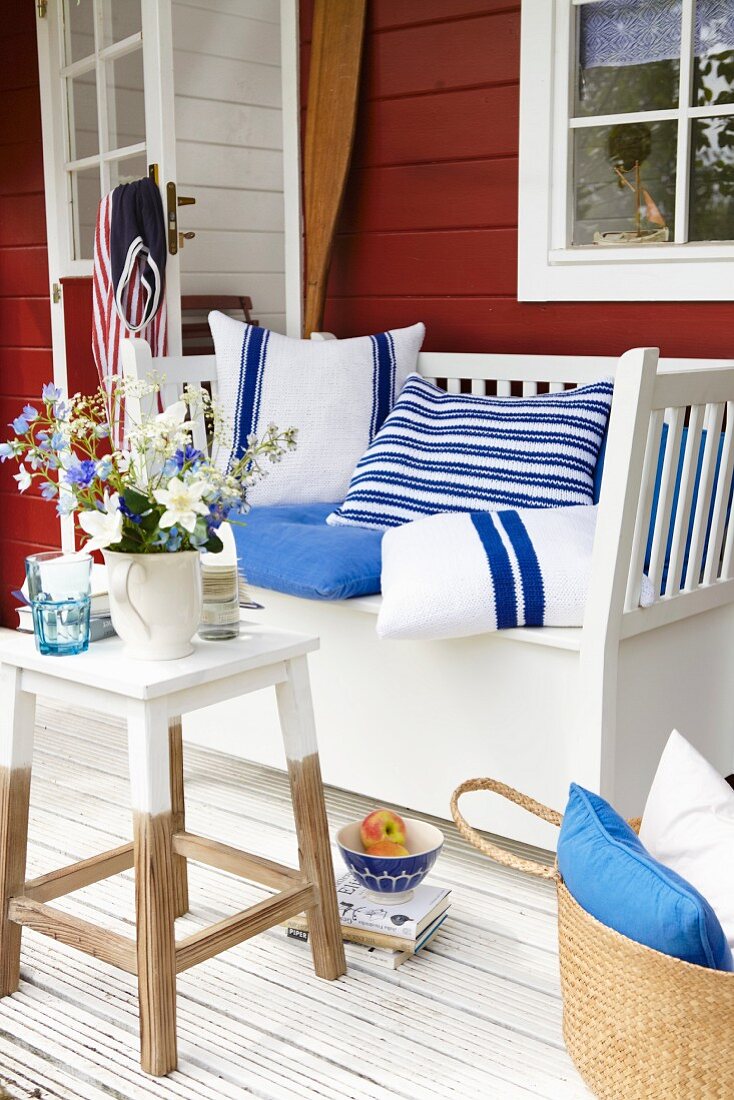 Flowers on a side table and homemade blue and white cushions on a wooden bench on a summery terrace