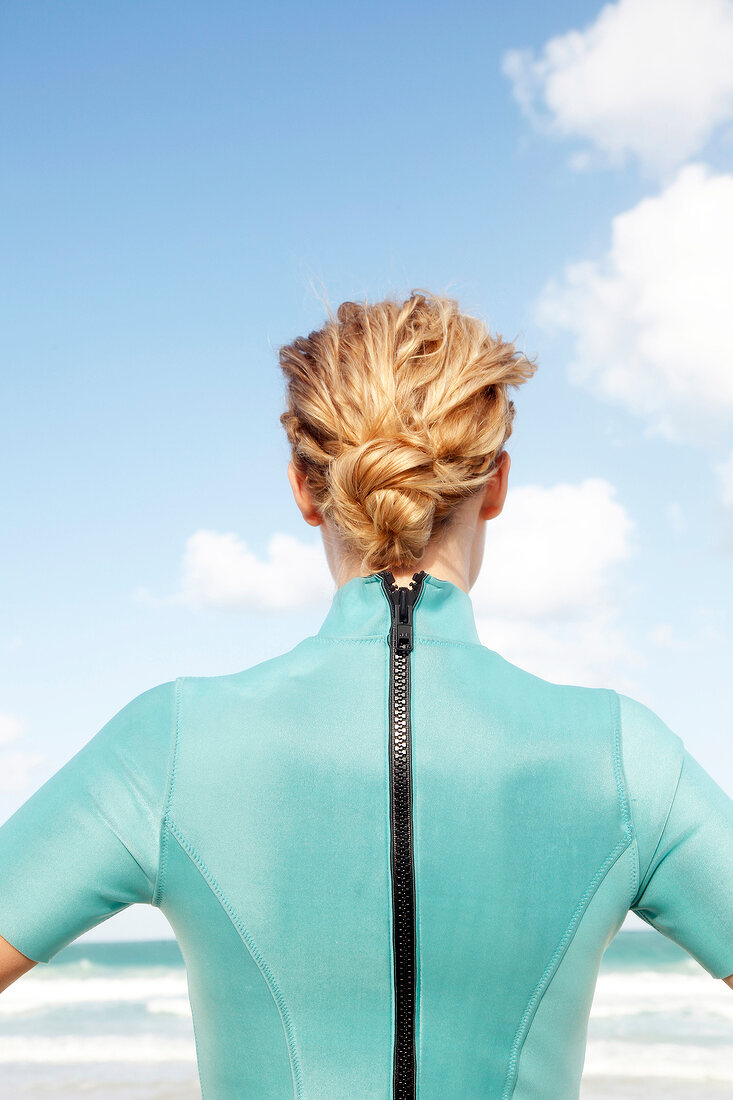 Woman with a bun in a green zipped wetsuit, from behind