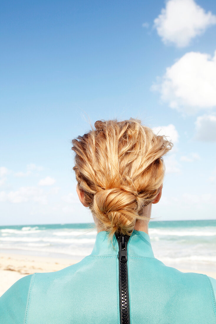 Woman with a bun in a green zipped wetsuit, from behind