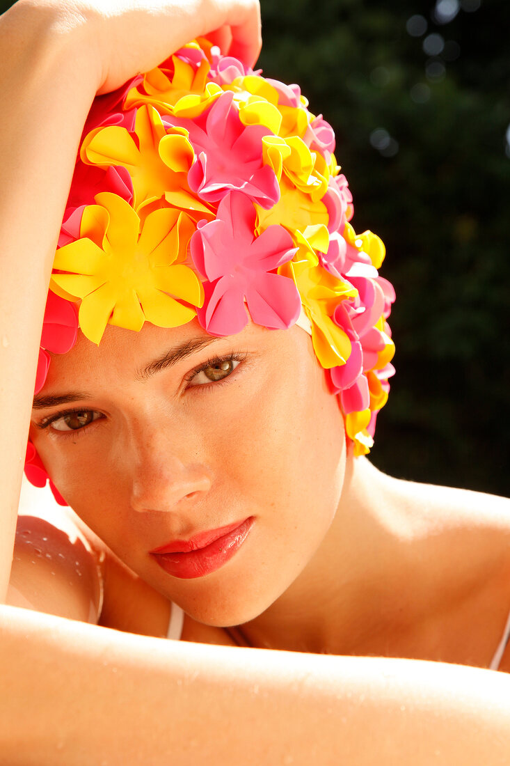 A woman wearing makeup with a colorful bathing cap looking into the camera